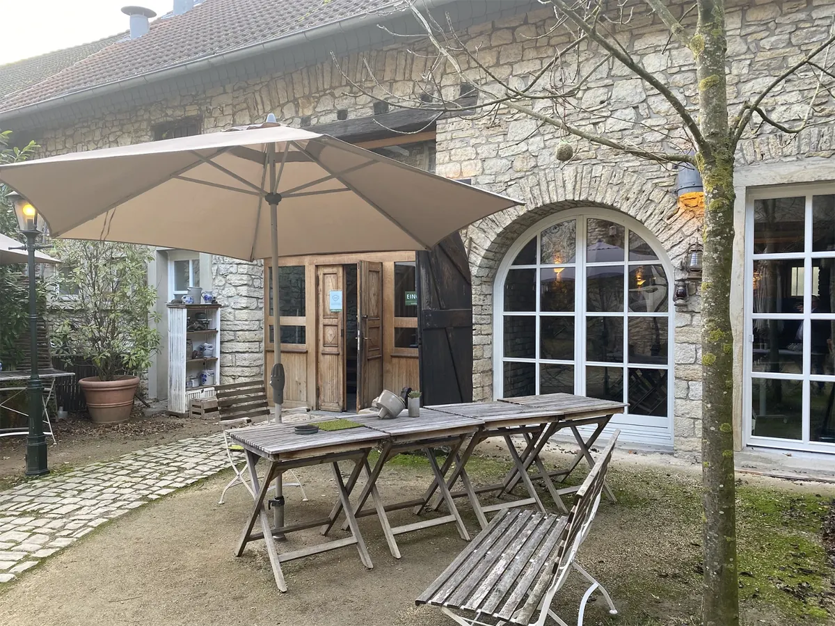 Hof des Alten Gutshofs mit Sonnenschirm, Holztischen und Rundbogenfenstern